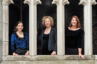 Three women from the Boston Camerata pose for the photo among architectural columns