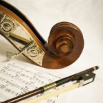Wooden top of a violin curls elegantly over a sheet of music and bow