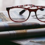 A pair of reading glasses sitting on top of a small stack of newspaper sections.